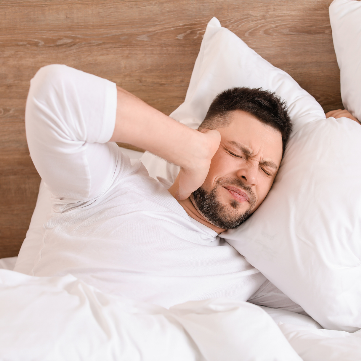 A man holds his ear in bed at night, as he is suffering from tinnitus